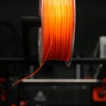 Close-up of an orange 3D printer filament spool in a workshop setting, highlighting innovation and design.