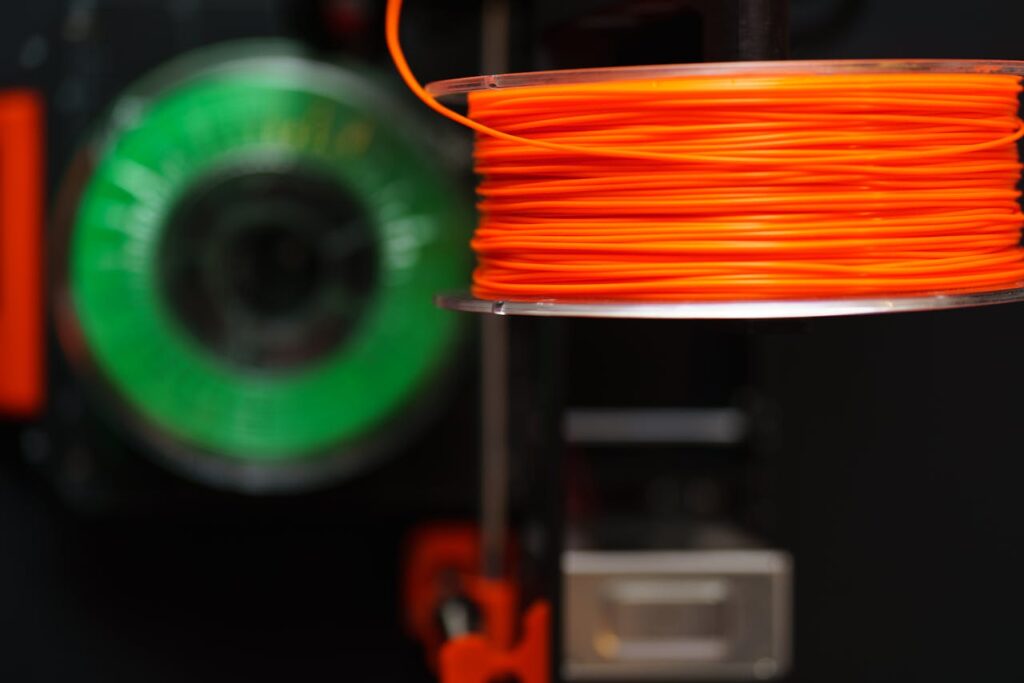 pexels-photo-31353177 Detailed view of orange and green 3D printer filament spools, perfect for creative and industrial projects.