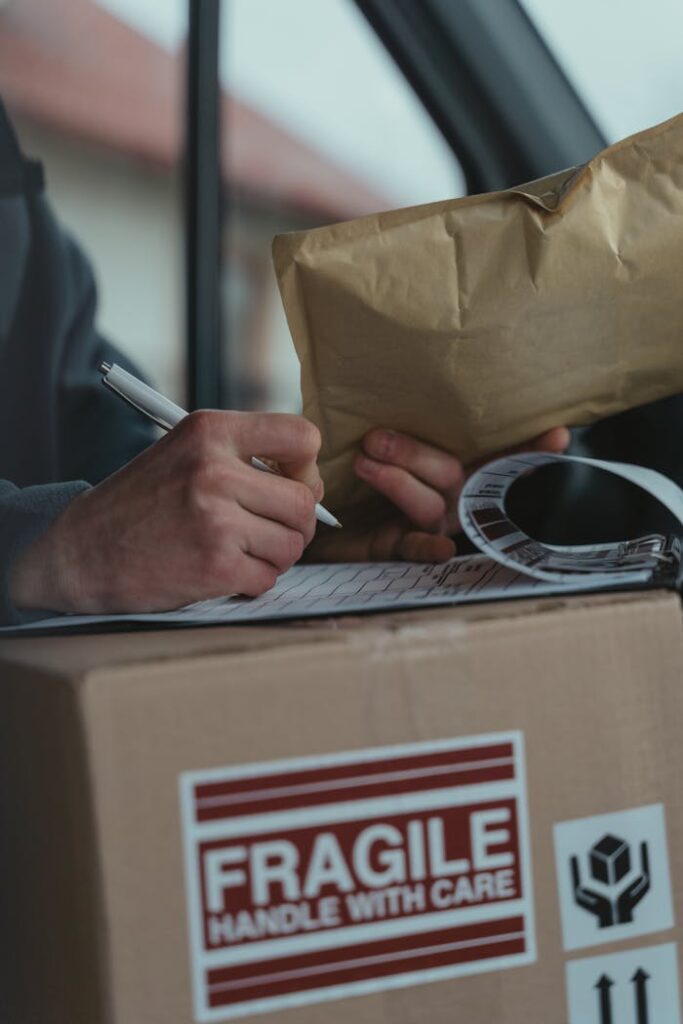 pexels-photo-6169858 Close-up of a courier writing on a clipboard with a fragile package inside a vehicle.